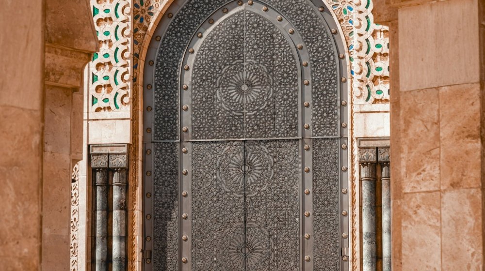 A visitor standing in front of one of the Hassan II Mosque's huge ornamented bronze doors, dwarfed by its scale