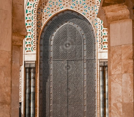 A visitor standing in front of one of the Hassan II Mosque's huge ornamented bronze doors, dwarfed by its scale