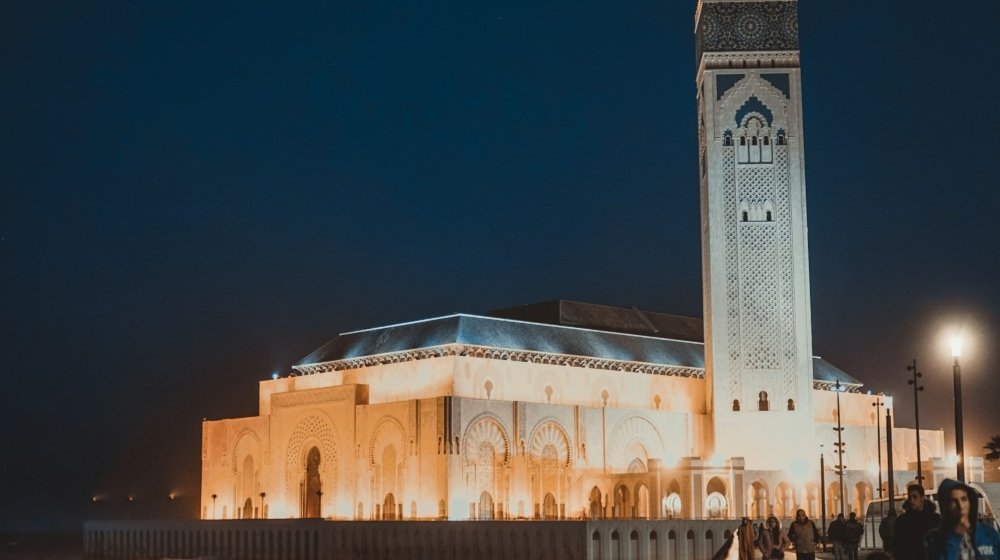 People walking past a floodlit stone building on a Casablanca street after dark