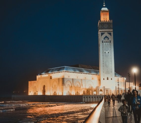 People walking past a floodlit stone building on a Casablanca street after dark