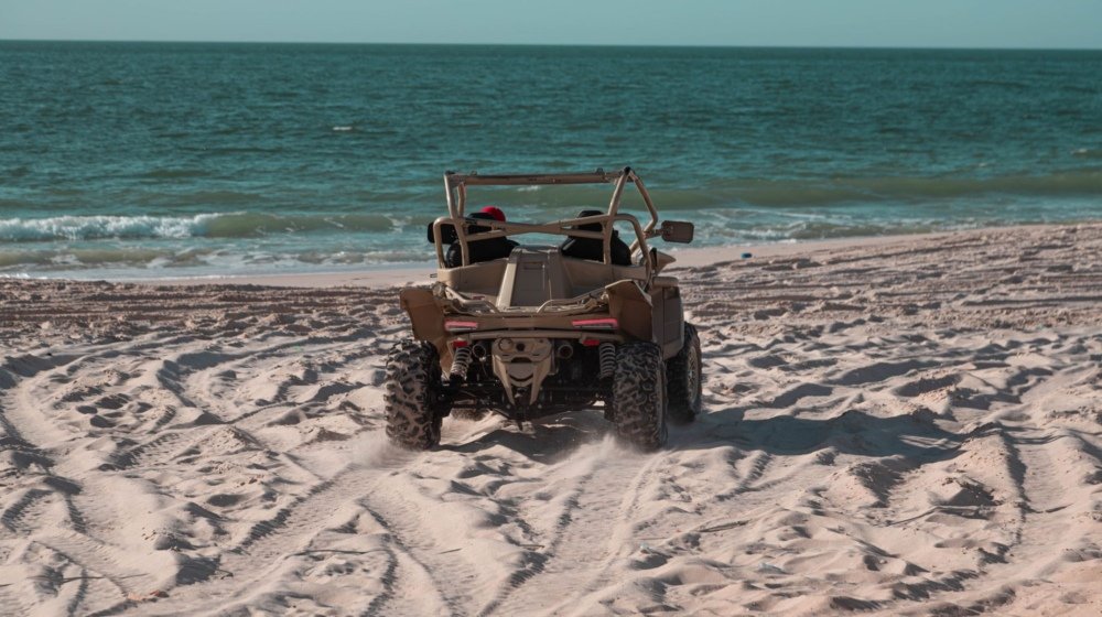 A beach buggy being driven across wet sand with ocean waves breaking directly behind it