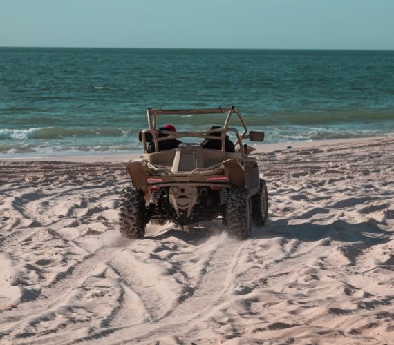 A beach buggy being driven across wet sand with ocean waves breaking directly behind it