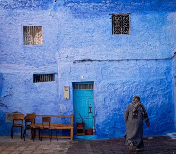 A person walking past a vivid blue-washed wall in a narrow street of Chefchaouen