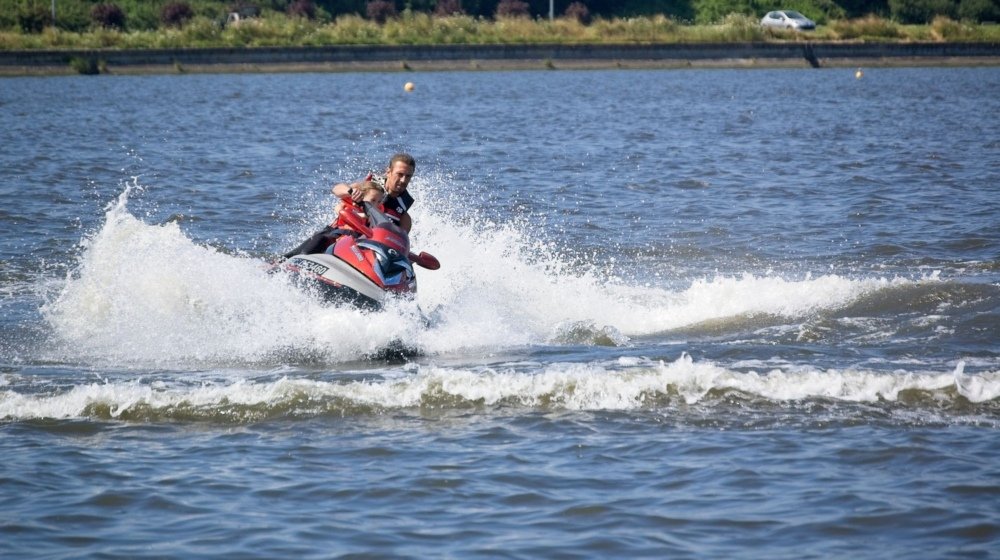 A man riding a jet ski at speed across open water, spray flying behind him