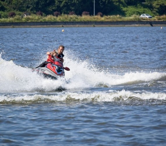 A man riding a jet ski at speed across open water, spray flying behind him