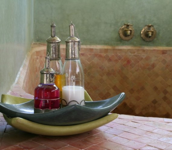 Interior of a traditional Moroccan hammam with tiled walls and bottles of massage and treatment oils set out ready for a bath ritual
