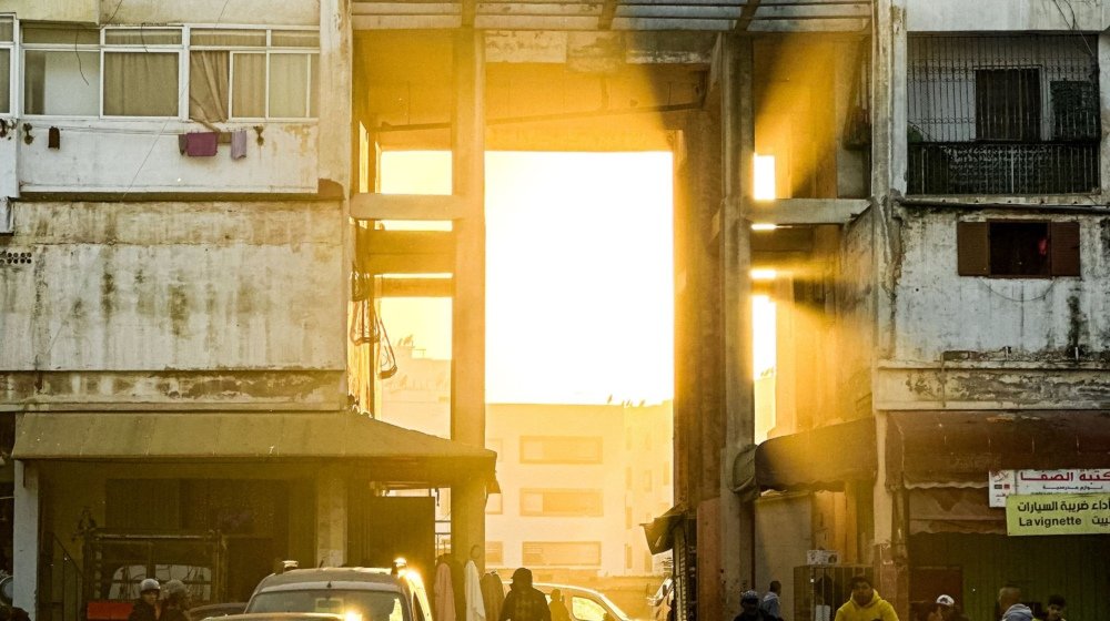 Pedestrians walking down a Casablanca street with low morning sunlight beaming between the buildings