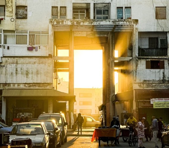 Pedestrians walking down a Casablanca street with low morning sunlight beaming between the buildings
