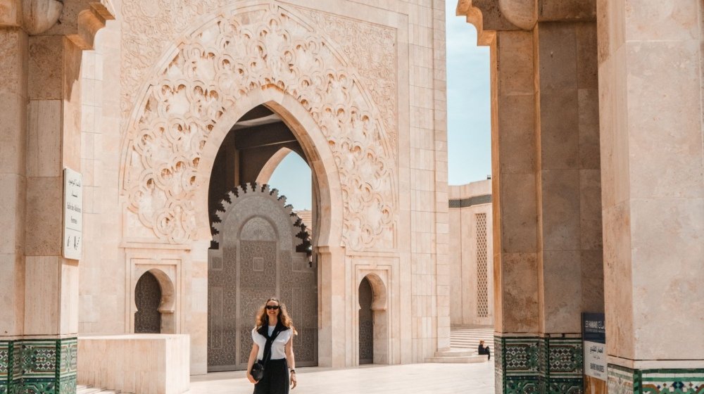 A visitor walking through the intricately carved and tiled arcades of the Hassan II Mosque in Casablanca