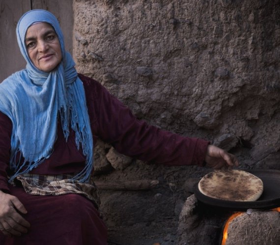 Moroccan woman baking traditional flatbread over an open stove in the Ourika Valley near Marrakech