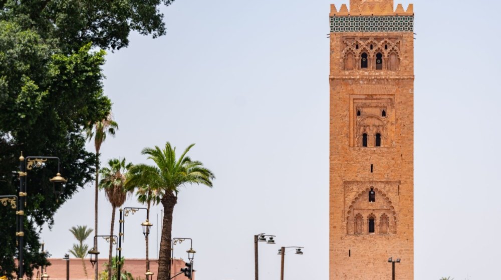 Green horse-drawn caleches with white horses lined up for sightseeing tours below the ochre Koutoubia minaret in Marrakech.