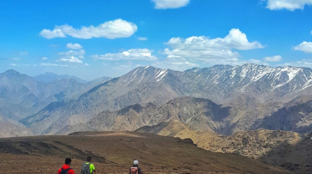 A group walking a dirt mountain path with the Atlas range rising behind them