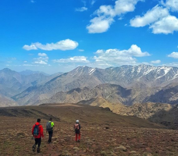 A group walking a dirt mountain path with the Atlas range rising behind them
