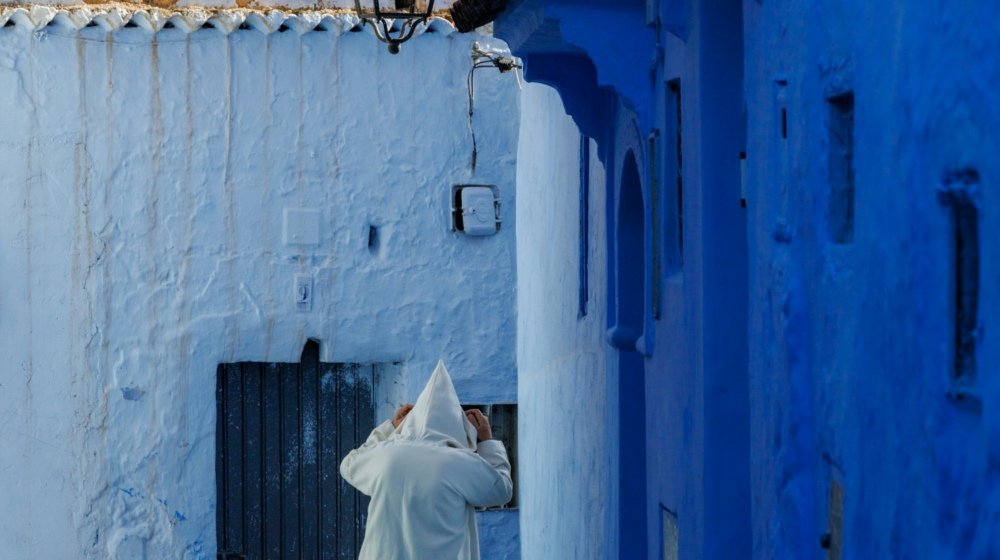 A figure in a white robe walking down a narrow blue-washed street in Chefchaouen