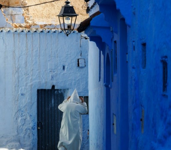 A figure in a white robe walking down a narrow blue-washed street in Chefchaouen