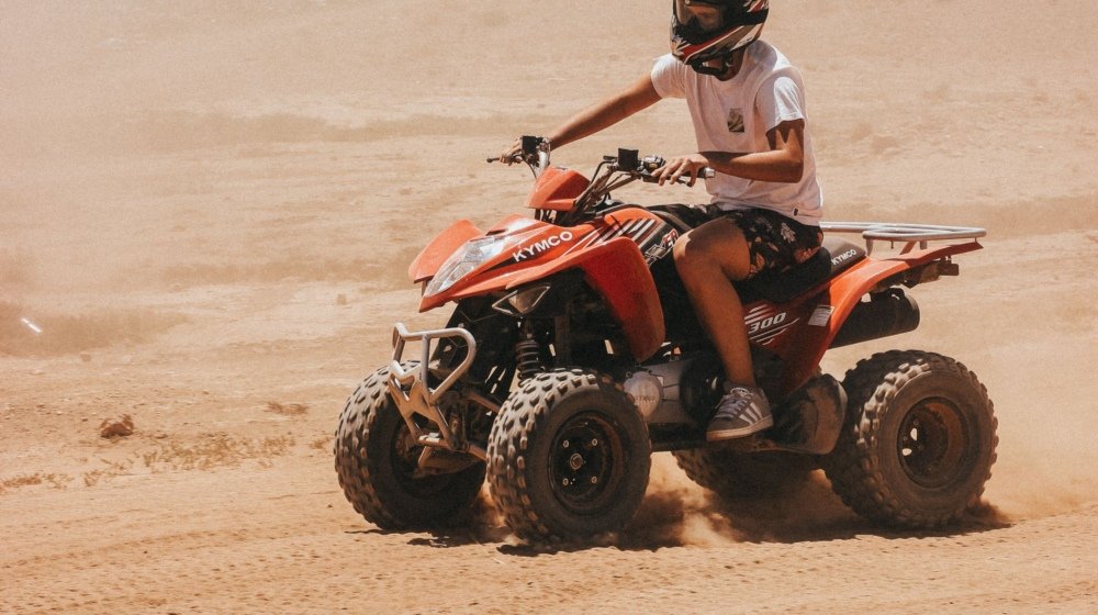 A rider on an orange quad bike powering across the dusty rocky desert outside Marrakech, throwing up a trail of sand