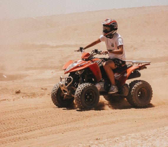 A rider on an orange quad bike powering across the dusty rocky desert outside Marrakech, throwing up a trail of sand