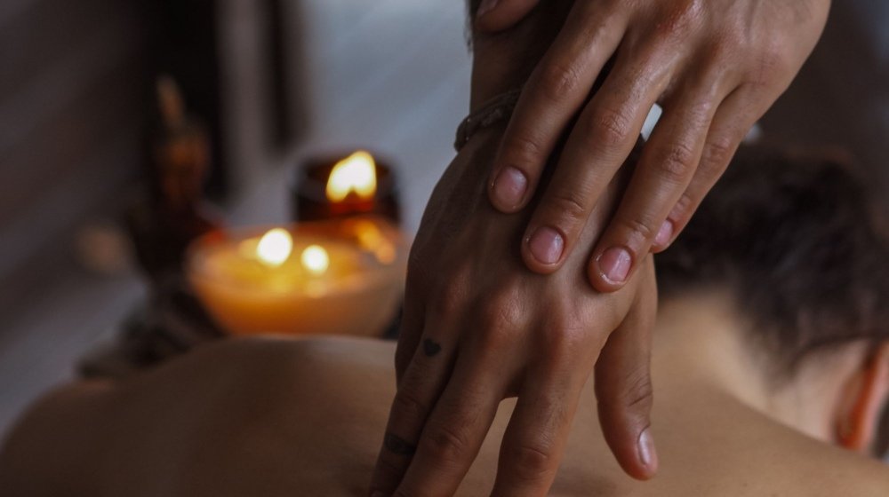 A therapist's hands working along a client's back during a massage, with candles glowing softly in the background