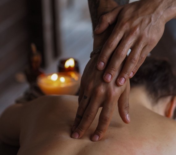 A therapist's hands working along a client's back during a massage, with candles glowing softly in the background