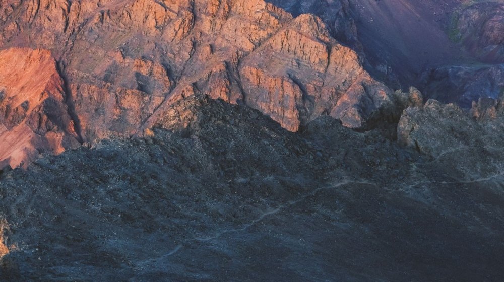 A line of trekkers crossing a rocky slope in the Moroccan mountains as first light hits the red rock face above