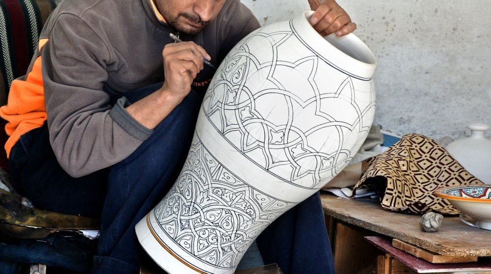 A Moroccan artisan in Fès painting intricate detail onto a large clay vase in his pottery workshop