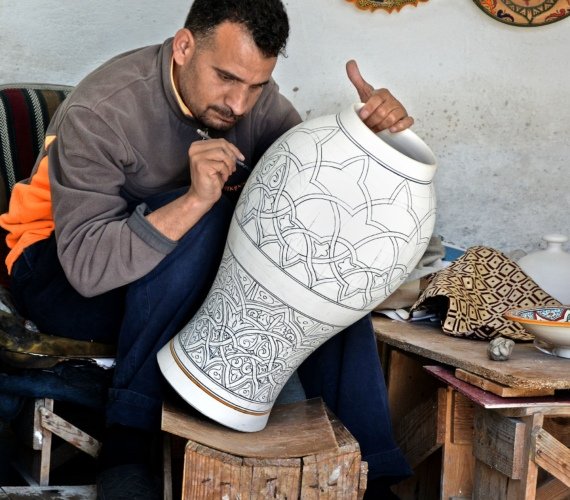 A Moroccan artisan in Fès painting intricate detail onto a large clay vase in his pottery workshop