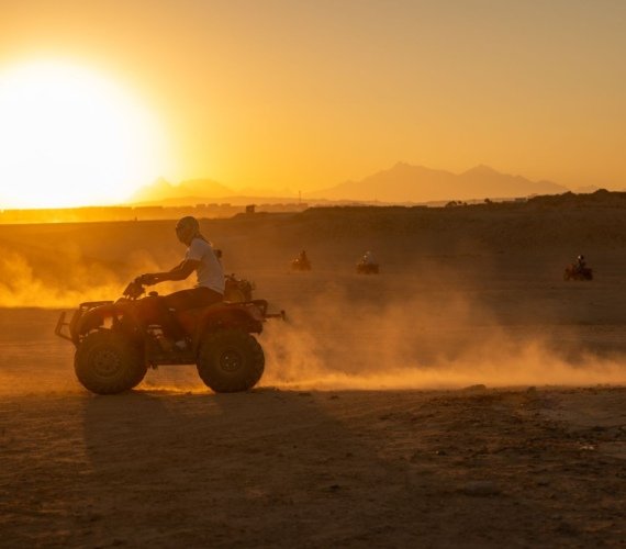 A group of quad bike riders crossing sand dunes in golden low sunlight with dust catching the light